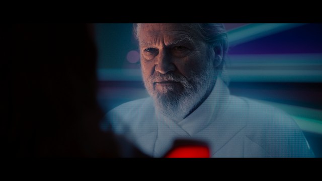 A close-up of an elderly man with a beard and white attire, appearing serious and contemplative, set against a colorful, futuristic background.