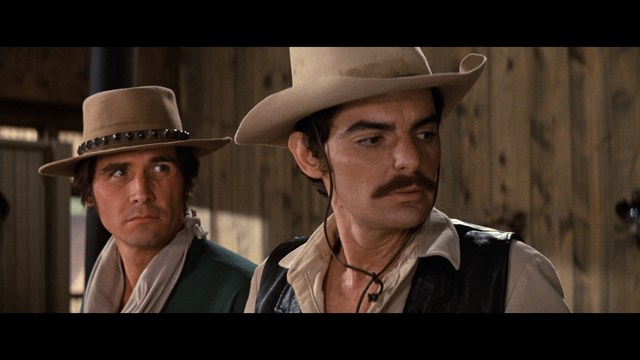 A woman with long dark hair resting her chin on her hand, looking pensively off to the side. In the background, various kitchen appliances and items are visible.