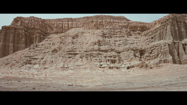 A woman sitting at a restaurant table, resting her chin on her hand while reading a newspaper.