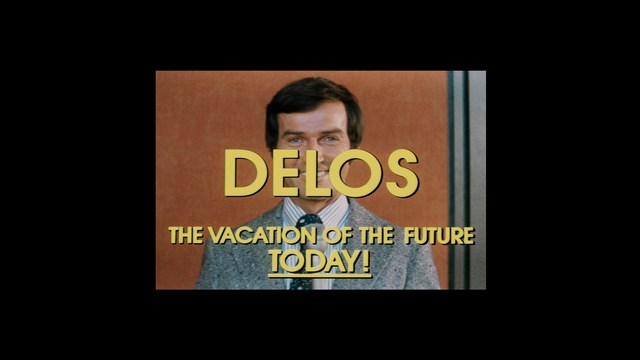 A still from a movie featuring a man standing on a boardwalk in front of an arcade with signs for Skeeball, saltwater taffy, and various attractions.