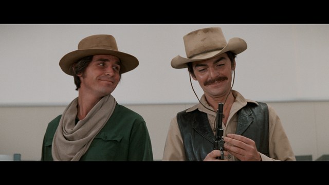 Statue of a smiling figure resembling Jesus, giving a thumbs up gesture, set against a colorful backdrop with signs related to Catholicism.