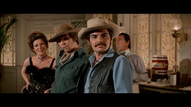 A close-up shot of a man with a distressed expression, featuring dark hair and wearing a blue hoodie, against a softly lit background.