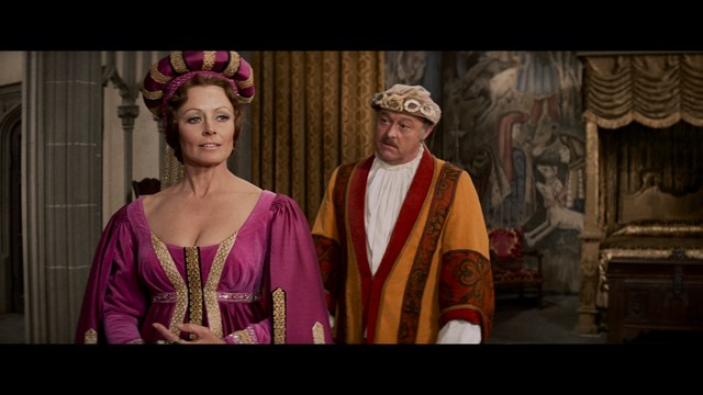 A scene from a movie featuring three characters standing on a bridge with a lush green landscape in the background.