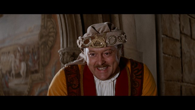 A scene featuring a man with short hair and a beard, wearing a brown jacket and purple shirt, standing outside a restaurant with bright yellow walls and a cartoon cow logo.