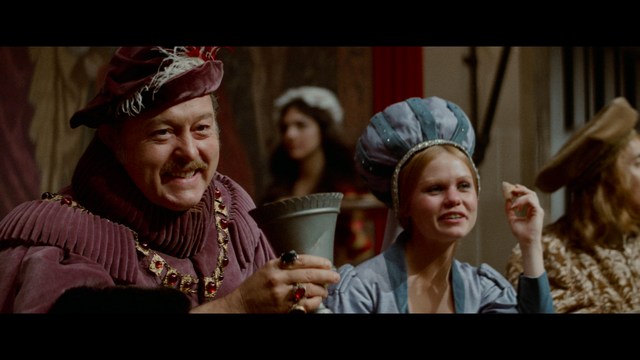 A golden trophy statue of a goblin-like character positioned on a wooden table in an office setting, with large windows and a building facade visible in the background.