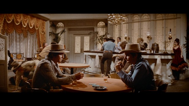 A man with short hair and a beard sits at a table, looking surprised or excited while holding a bottle.