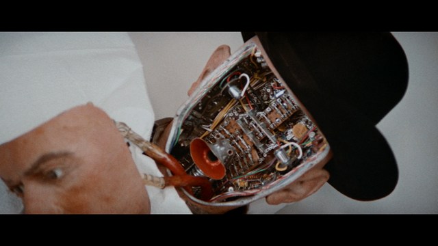 Close-up of a woman with long black hair sitting in a restaurant, looking concerned. A colorful painting is visible in the background, along with red bar stools.