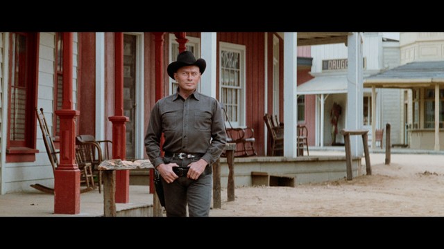 Two young men are looking at something off-camera, standing inside a building with bright lighting and seating areas visible in the background.