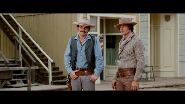 A close-up shot of a man wearing a white suit and a white hat, looking intently at someone in a retail store filled with merchandise.