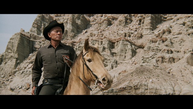 A man with dark, styled hair and a subtle smile seated at a restaurant table, with blurred diners in the background.