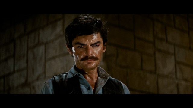 A shocked man with long hair and a baseball cap sitting in a bar, looking surprised.