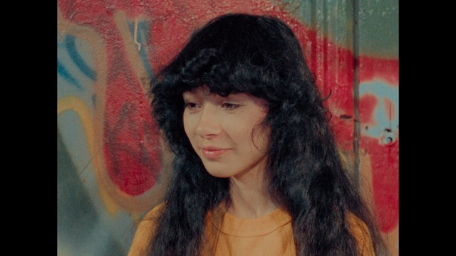 A still from a movie featuring a man standing on a boardwalk in front of an arcade with signs for Skeeball, saltwater taffy, and various attractions.