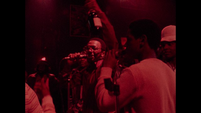 A group of people standing in a church, with a focus on a woman in a striped blazer looking up, while others are holding books or looking ahead.