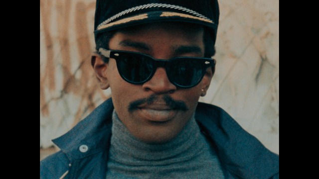 Two characters sitting in a diner, one wearing a blue beanie with 'SNOOGANS' and the other wearing a cap, both looking intently at something off-screen.