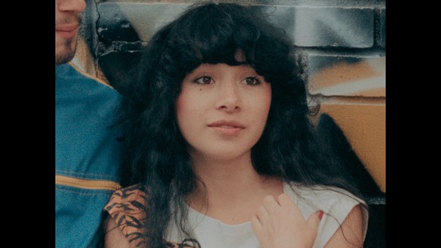 A worried woman stands on a deserted road, looking shocked or distressed as she gazes into the distance.