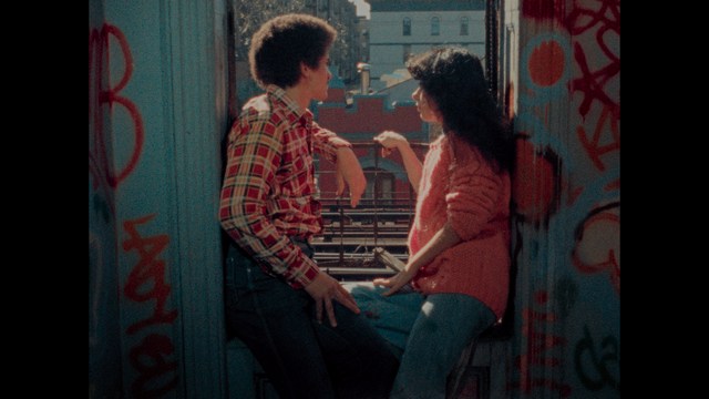 A golden trophy statue of a goblin-like character positioned on a wooden table in an office setting, with large windows and a building facade visible in the background.