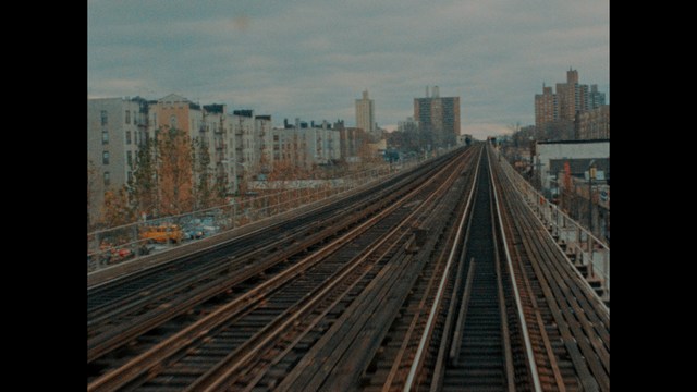Close-up of a man with a serious expression, seated in a dimly lit area, with soft lighting from background lamps.