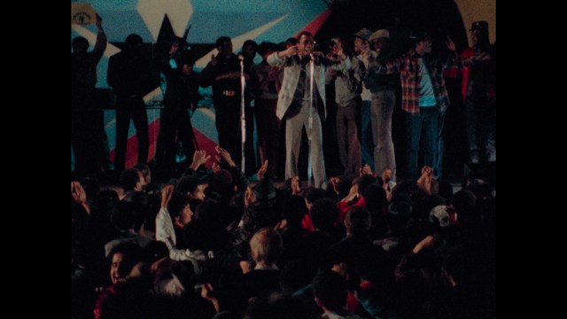 Two figures walking on a road towards a blue 'Welcome to New Jersey' sign.